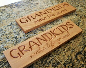 May include: Two wooden signs with the text "Grandkids make life grand" carved into the surface. The signs are made of light brown wood and have a rustic look.
