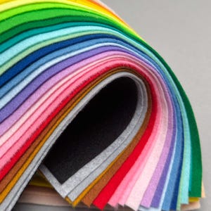 Könnte beinhalten: Ein Stapel rechteckiger Filzblätter, die in einer geschwungenen, kaskadierenden Formation angeordnet sind. Die Sammlung umfasst ein breites Farbspektrum, darunter Rot-, Orange-, Gelb-, Grün-, Blau-, Violett-, Rosa-, Braun-, Grau- und Schwarztöne.