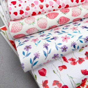 May include: A stack of decorative faux leather sheets with various patterns. Designs include pink leopard print, red and pink hearts, pink strawberries, purple flowers, and red poppies. The sheets are stacked on a gray surface.