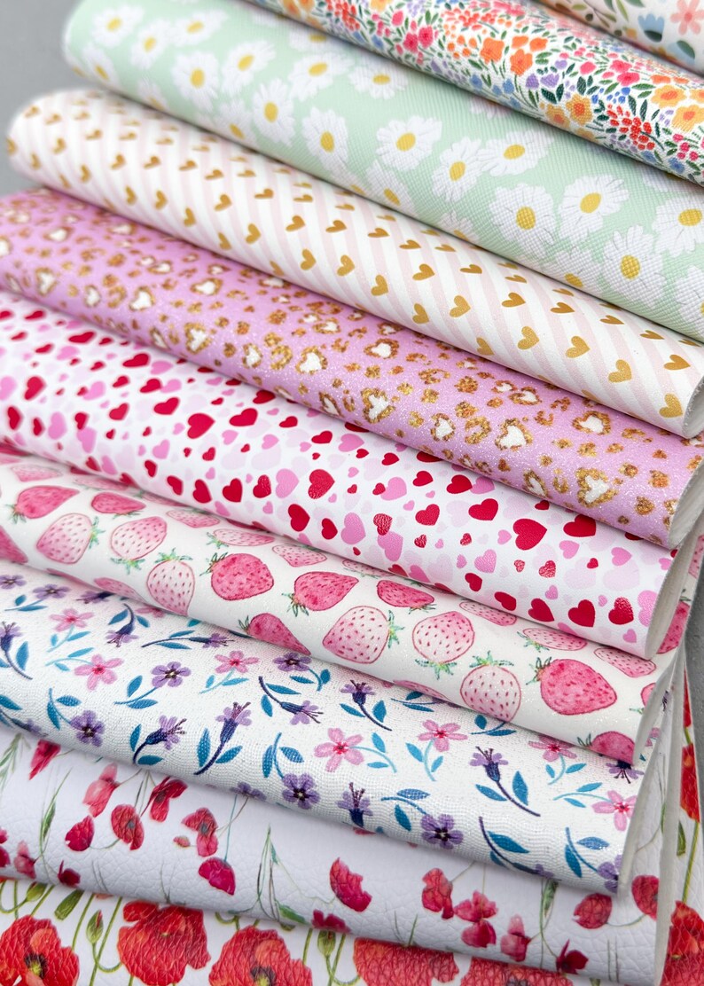 May include: A stack of patterned faux leather sheets. Designs include daisies, hearts, strawberries, and floral patterns in various colors like pink, white, and green. The sheets are suitable for crafting and DIY projects.