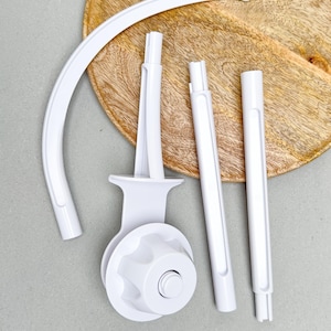 May include: White baby mobile components, including a curved arm, support rods, and a circular base with a knob. The pieces are arranged on a light gray surface with a wooden background.