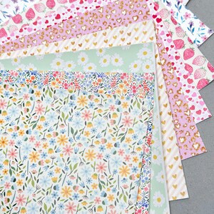May include: A collection of patterned papers with various designs, including strawberries, hearts, daisies, and floral patterns. The papers feature a range of colors, such as pink, white, gold, and green. The papers are arranged in a fan shape, showcasing the different designs.