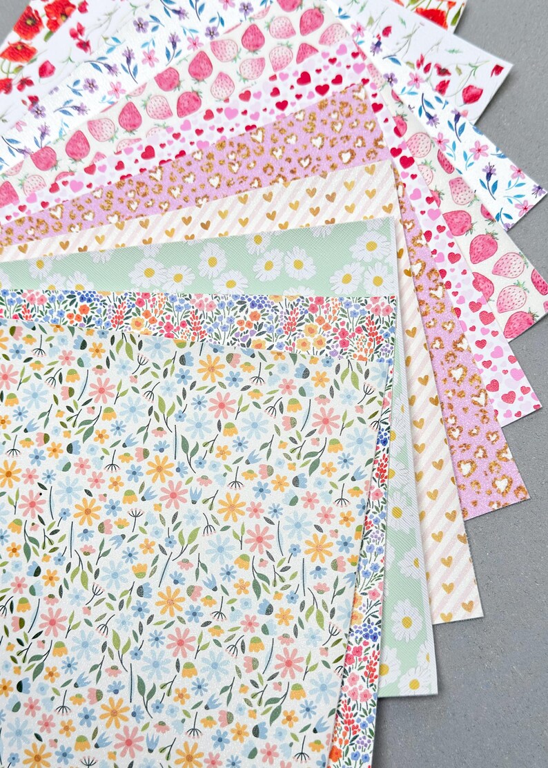 May include: A collection of patterned papers with various designs, including strawberries, hearts, daisies, and floral patterns. The papers feature a range of colors, such as pink, white, gold, and green. The papers are arranged in a fan shape, showcasing the different designs.