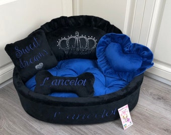 May include: A black and blue dog bed with a crown design and the name "Lancelot" embroidered on it. The bed has a heart-shaped pillow and a pillow with the text "Sweet dreams".