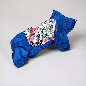 May include: A blue dog raincoat with a floral print panel on the back. The floral pattern includes pink, red, and blue flowers on a white background. The raincoat has a hood and elastic cuffs.