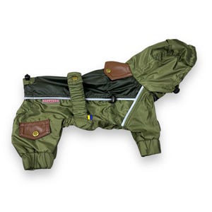 May include: Olive green dog jacket with a hood, brown leather-like accents, and the text "HAPPYDOG". The jacket has a black panel on the back and a reflective stripe. Features include pockets and elastic cuffs. A stylish and functional dog apparel item.