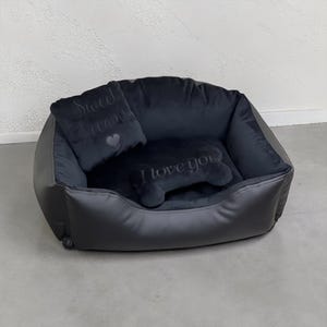 May include: A black pet bed with a plush interior and a faux leather exterior. Includes a square pillow with "Sweet dreams" embroidered on it and a bone-shaped pillow with "I love you" embroidered on it. The bed is designed for small dogs or cats.