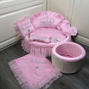 May include: Pink dog bed with a crown and the words "Princess" and "Sweet Dreams". The bed has a pink and white ruffled skirt. There is also a pink blanket with the word "Princess" and a pink and white dog toy with the words "My Toys".