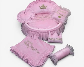 May include: A pink pet bed with ruffled tulle trim, featuring a gold embroidered crown and the text Ming Ming. Includes a heart-shaped pillow, a square pillow with the text Sweet dreams, a crown-shaped pillow, and a blanket with xoxo Dolly Maltese.