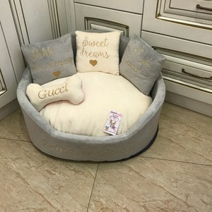 May include: A gray and white dog bed with a bone-shaped pillow and three pillows with embroidered text. The pillows say "Shh... I'm sleeping", "Sweet dreams", and "Gucci". The bed is embroidered with "Princess Gucci".