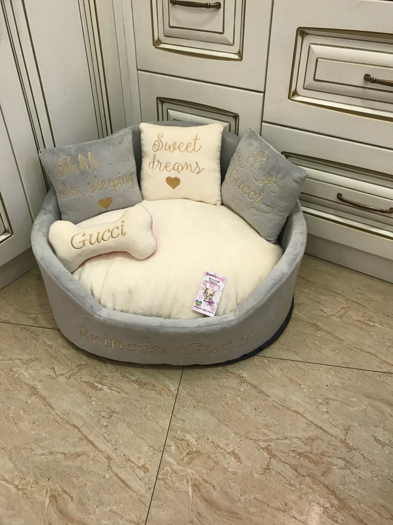 May include: A gray and white dog bed with a bone-shaped pillow and three pillows with embroidered text. The pillows say "Shh... I'm sleeping", "Sweet dreams", and "Gucci". The bed is embroidered with "Princess Gucci".