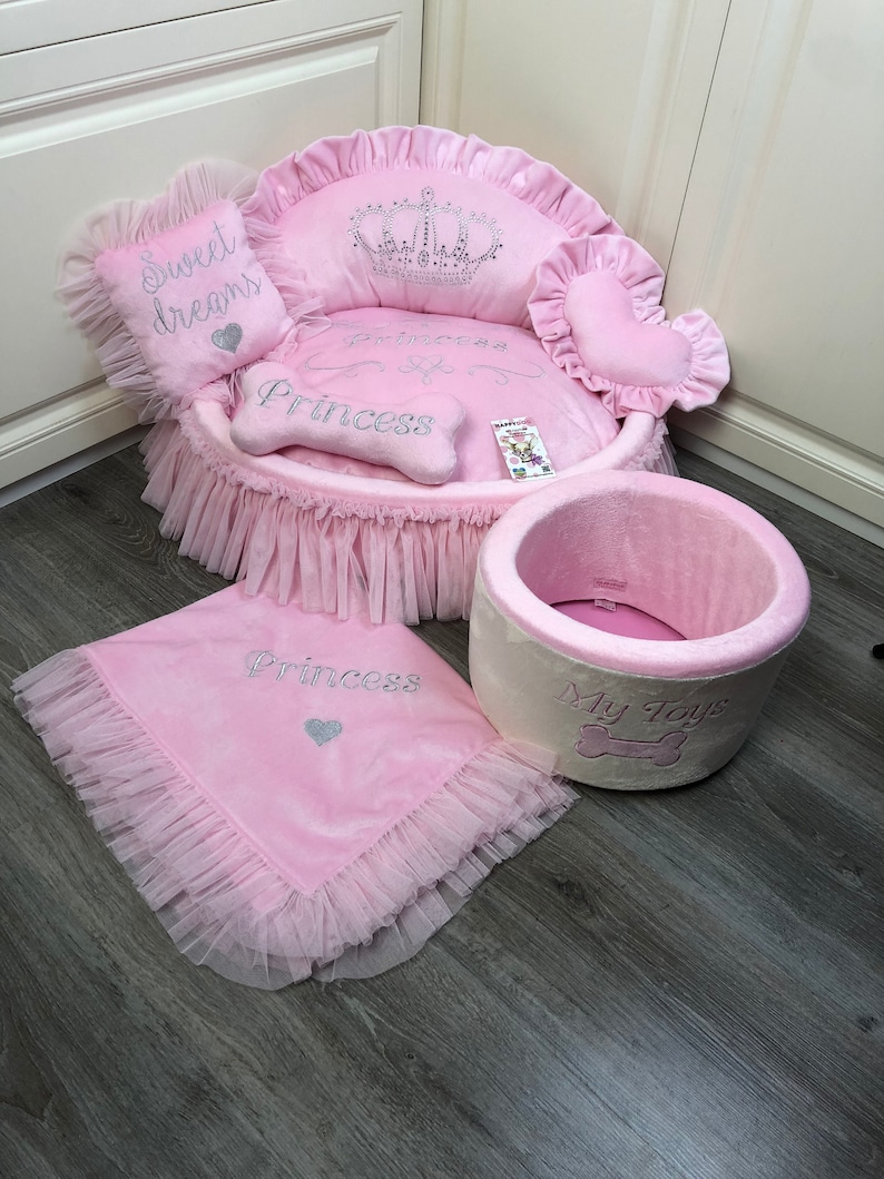 May include: Pink princess dog bed with a crown, a bone-shaped pillow, and a separate pink and white dog bed with the words "My Toys".