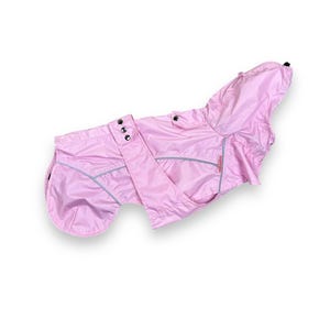 May include: A light pink dog raincoat with a hood. The dog jacket has a reflective trim and adjustable straps with three metal snaps. The dog coat is designed to protect a dog from the rain.