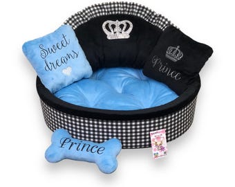 May include: A dog bed with a black and white checkered exterior, a blue interior, and two pillows. One pillow says "Sweet dreams" and the other says "Prince". A blue bone-shaped toy says "Prince". A crown is embroidered on the bed.