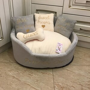 May include: A gray and white dog bed with a bone-shaped pillow that says "Gucci" and three pillows with embroidered text: "Shhh... I'm sleeping", "Sweet dreams", and "Gucci". The bed is embroidered with "Princess Gucci".