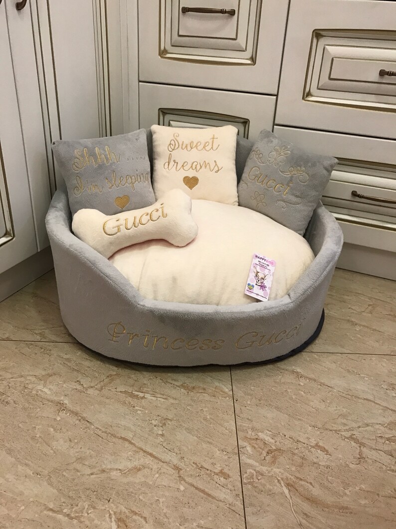 May include: A gray and white dog bed with a bone-shaped pillow that says "Gucci" and three pillows with embroidered text: "Shhh... I'm sleeping", "Sweet dreams", and "Gucci". The bed is embroidered with "Princess Gucci".