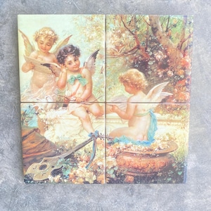May include: Set of four decorative ceramic tiles featuring cherubic angels in a classical, romantic style. Each tile depicts a different scene with angels, musical instruments, and floral elements, in soft pastel colors.