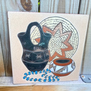 May include: A ceramic tile with a Southwestern design featuring a black and white pottery vase, a brown and white pottery bowl, a woven basket, and a blue and white beaded necklace.