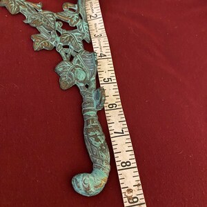 Pode incluir: Um suporte decorativo de metal verde com um design de videira e folhas. O suporte mede aproximadamente 20 cm de comprimento.