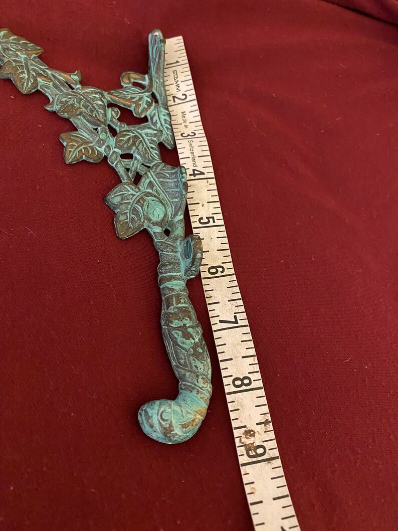 Pode incluir: Um suporte decorativo de metal verde com um design de videira e folhas. O suporte mede aproximadamente 20 cm de comprimento.