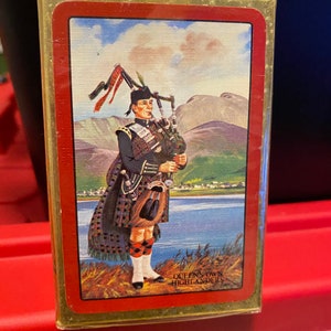 May include: A deck of playing cards featuring a Scottish bagpiper in traditional attire, set against a backdrop of a lake and mountains. The text "QUEEN'S OWN HIGHLANDERS" is visible on the card.