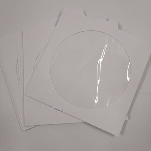 May include: A stack of white CD/DVD sleeves with a clear, circular window. The sleeves are made of cardstock and are designed to hold optical discs. The clear window allows for easy viewing of the disc label.