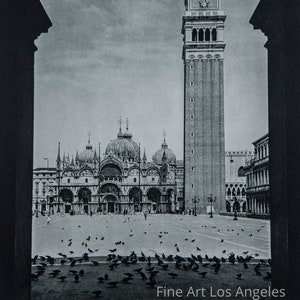 Pode incluir: Uma fotografia a preto e branco de uma torre alta e estreita com um telhado pontiagudo, vista através de um arco. A torre está no centro da imagem, e um grande edifício com uma cúpula é visível no fundo. A imagem é tirada de um ângulo baixo, e a torre parece muito alta.