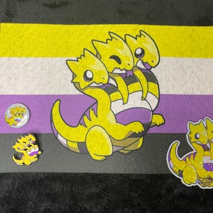Peut inclure: Un drapeau de fierté jaune, violet et blanc avec un motif de dragon à trois têtes. Le dragon est jaune avec des rayures violettes et blanches. Il y a deux versions plus petites du motif du dragon sur le drapeau, l'une sous forme de bouton et l'autre sous forme d'autocollant.