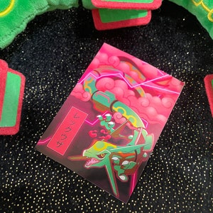 May include: A green and red Pokemon card featuring a pink and green dragon-like creature. The card has Japanese text that reads "ザクンシ" on the left side.