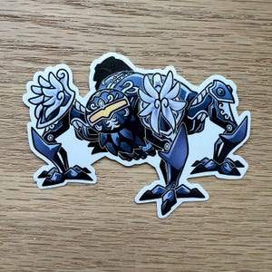 May include: A sticker featuring a stylized, dark blue creature with intricate details. The creature has a flower-like design on its chest and a yellow visor. The sticker is on a wooden surface.