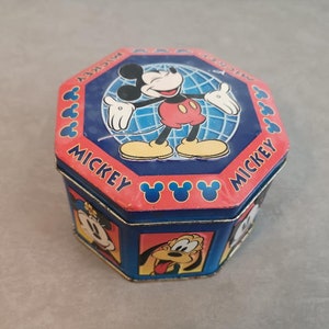 Peut inclure: Une boîte en métal octogonale bleue et rouge avec un motif Mickey Mouse. La boîte représente Mickey Mouse au centre, avec un globe derrière lui. Les mots "Mickey Mouse" sont imprimés sur la boîte.