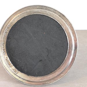 May include: A silver-colored round metal base with a black center and the text "EP ZINC ALLOY SILVER" inscribed around the edge.