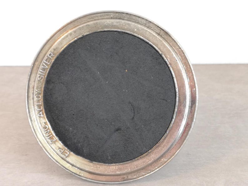 May include: A silver-colored round metal base with a black center and the text "EP ZINC ALLOY SILVER" inscribed around the edge.