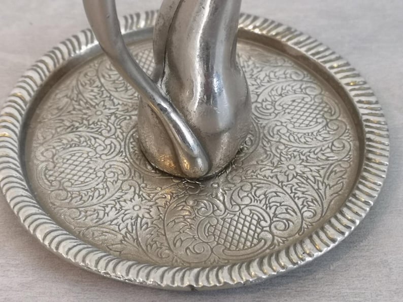 May include: A silver ring holder in the shape of a cat with a decorative, embossed tray. The tray has a floral pattern.