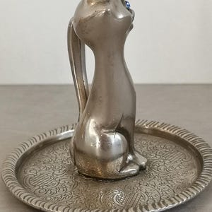 May include: Silver ring holder featuring a cat figurine with blue eyes sitting on a decorative tray.