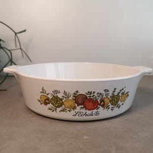 Op de afbeelding: Witte keramische bakvorm met een groen, geel en rood bloemmotief met groenten en de tekst "L'Echalote".