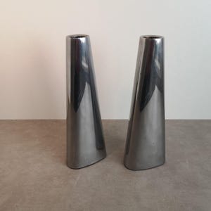 Op de afbeelding: Een paar zilveren metalen kaarsenstandaards met een driehoekige vorm.