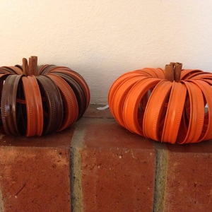 May include: Two pumpkins made from stacked orange and brown jar lids. The pumpkins are sitting on a brick surface.