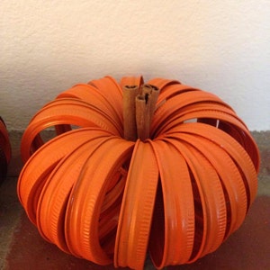 May include: Orange pumpkin made from stacked orange jar lids with a cinnamon stick stem.