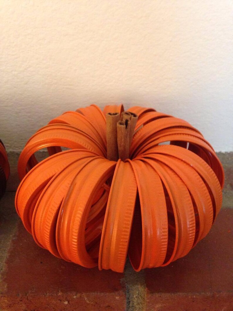 May include: Orange pumpkin made from stacked orange jar lids with a cinnamon stick stem.
