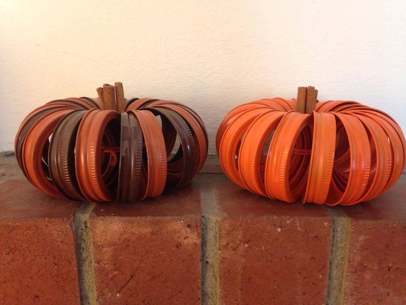 May include: Two pumpkins made from orange and brown jar lids. The pumpkins are sitting on a brick surface.