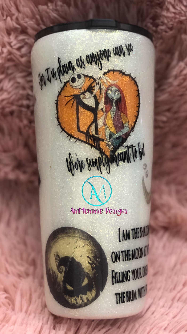 Puede incluir: Un vaso blanco con purpurina y tapa negra. El vaso presenta un gr&aacute;fico de Jack Skellington y Sally de la pel&iacute;cula Pesadilla antes de Navidad. El texto "For it is plain as anyone can see, we're simply meant to be!" est&aacute; impreso en el vaso. El texto "AmMommie Designs" tambi&eacute;n est&aacute; impreso en el vaso. El vaso tambi&eacute;n presenta un gr&aacute;fico de Jack Skellington en la luna con el texto "I am the shadow on the moon at night, filling your dreams with the brim with fright."