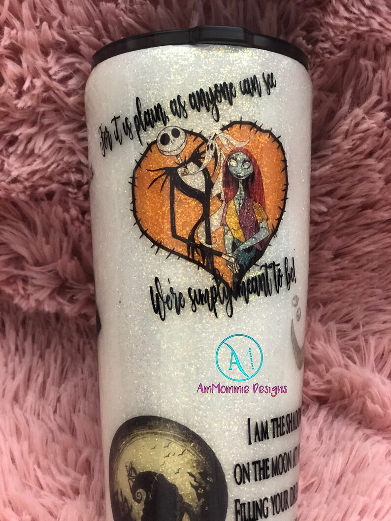 Puede incluir: Un vaso blanco con purpurina y una tapa negra. El vaso presenta un gr&aacute;fico de Jack Skellington y Sally de la pel&iacute;cula Pesadilla antes de Navidad. El texto "For it is plain as anyone can see, we're simply meant to be" est&aacute; impreso en el vaso. El vaso tambi&eacute;n presenta un gr&aacute;fico de luna con una silueta de Jack Skellington. El texto "I am the shadow on the moon at night, filling your dreams with fright" est&aacute; impreso en el vaso. El vaso est&aacute; decorado con un logotipo en blanco y negro que dice "AmMommie Designs".
