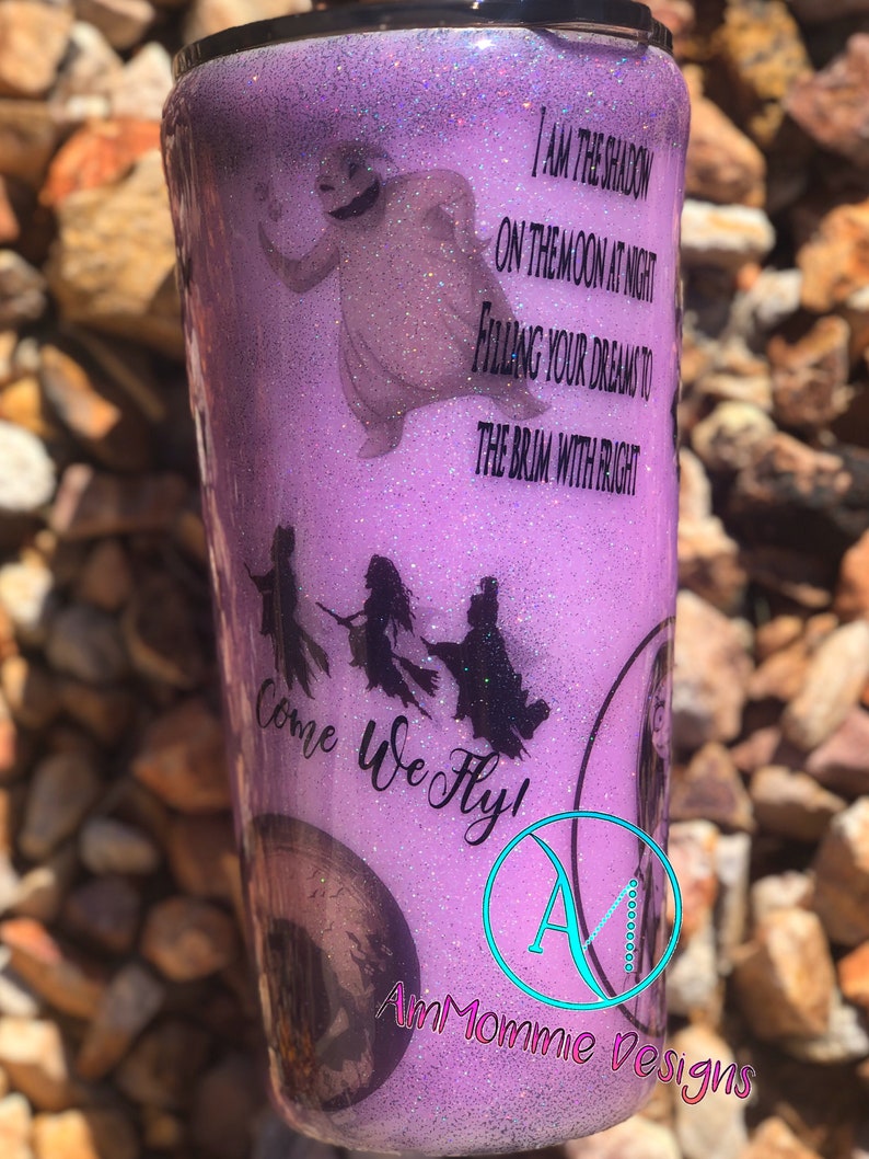 May include: Purple glitter tumbler with a silhouette of the Sanderson sisters from Hocus Pocus flying on broomsticks. The text "Come We Fly!" is written in black cursive. The tumbler also features a silhouette of the ghost from the movie "The Nightmare Before Christmas" and the text "I am the shadow on the moon at night filling your dreams to the brim with fright".