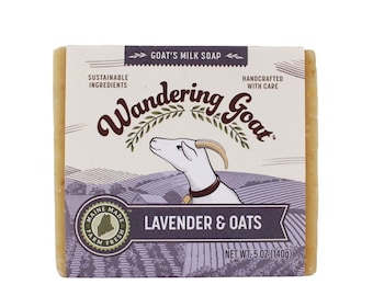 May include: A bar of goat's milk soap with a lavender and oat scent. The soap is packaged in a white box with a cartoon goat and the text "Wandering Goat". The soap is made with sustainable ingredients and handcrafted with care. The soap weighs 140 grams (5 ounces).