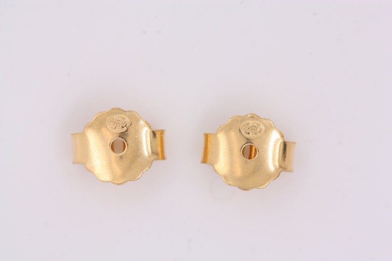 May include: Two gold-toned earring backs with a small hole in the center and a clasp on the side.