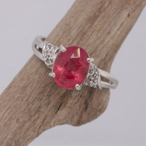 May include: A silver ring with a large oval-shaped red gemstone and smaller diamonds set in the band.