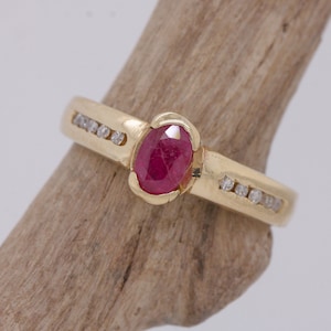 May include: A gold ring with a red oval ruby gemstone and a band of small diamonds.