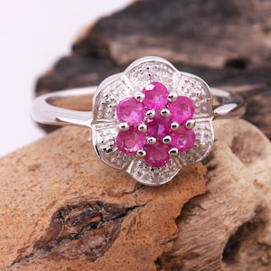 May include: A silver ring with a pink flower design. The flower is made of small pink gemstones surrounded by smaller white gemstones.