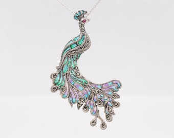 Puede incluir: Un collar con un colgante de plata en forma de pavo real con detalles de esmalte verde, azul y morado y un ojo de piedra preciosa roja. Las plumas de la cola del pavo real están detalladas con piedras de marcasita.